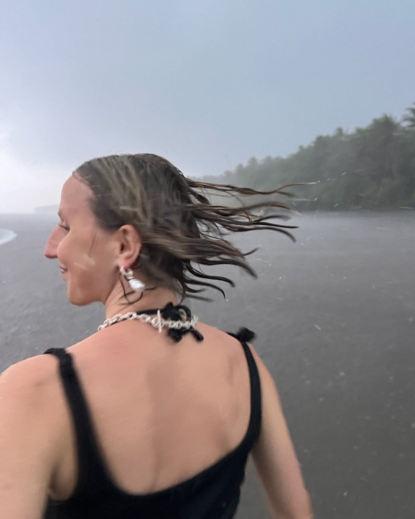 Frau mit künstlerischem Schmuck aus der Rope Kollektion von ORFÈVRE – Halskette und Ohrringe im modernen Design, fotografiert am Strand bei Regen, Juwelier Düsseldorf.